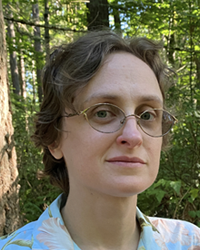 Heather, owner of Rainy Day Art, smiling for a picture in the woods.